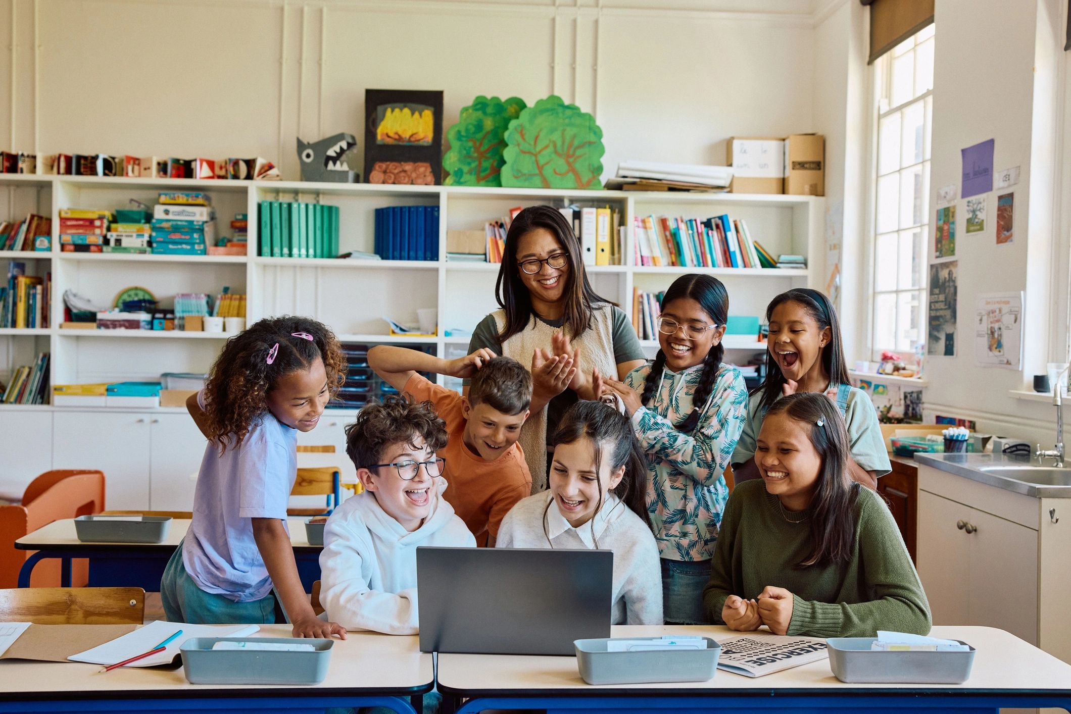 Teacher and preschool children gathered around a laptop in a modern classroom
